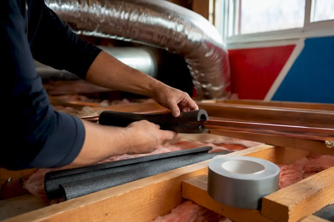 Hands installing foam insulation on pipes